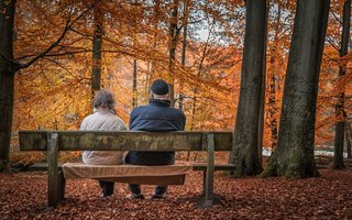 Rentnerpaar sitzt im herbstlichen Wald auf einer Bank.