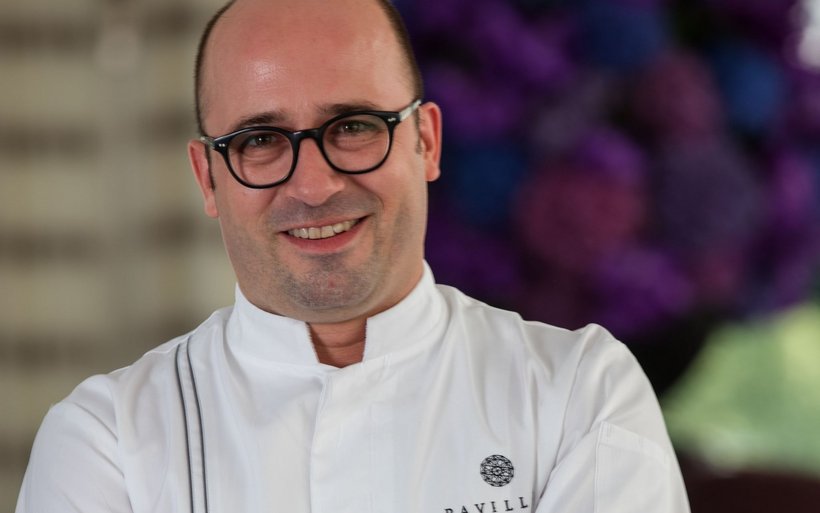 Portrait eines Mannes mit wenig Haaren und heller Hautfarbe. Er trägt eine dunkle, runde Brille und eine Kochweste.