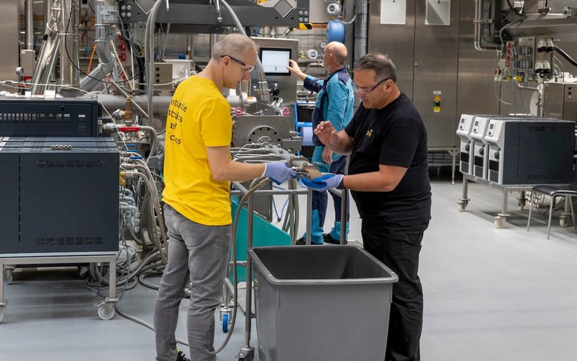 Zwei Männer hantieren in einer Produktionsstätte mit einem Schlauch.